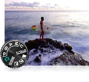 Nikon COOLPIX P900 photo of a surfer on jetties and mode dial showing full manual control